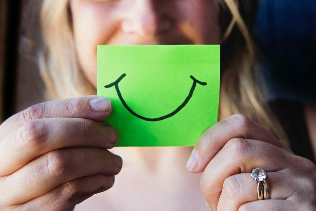 A woman holding a green post-it note with a smile drawn on it