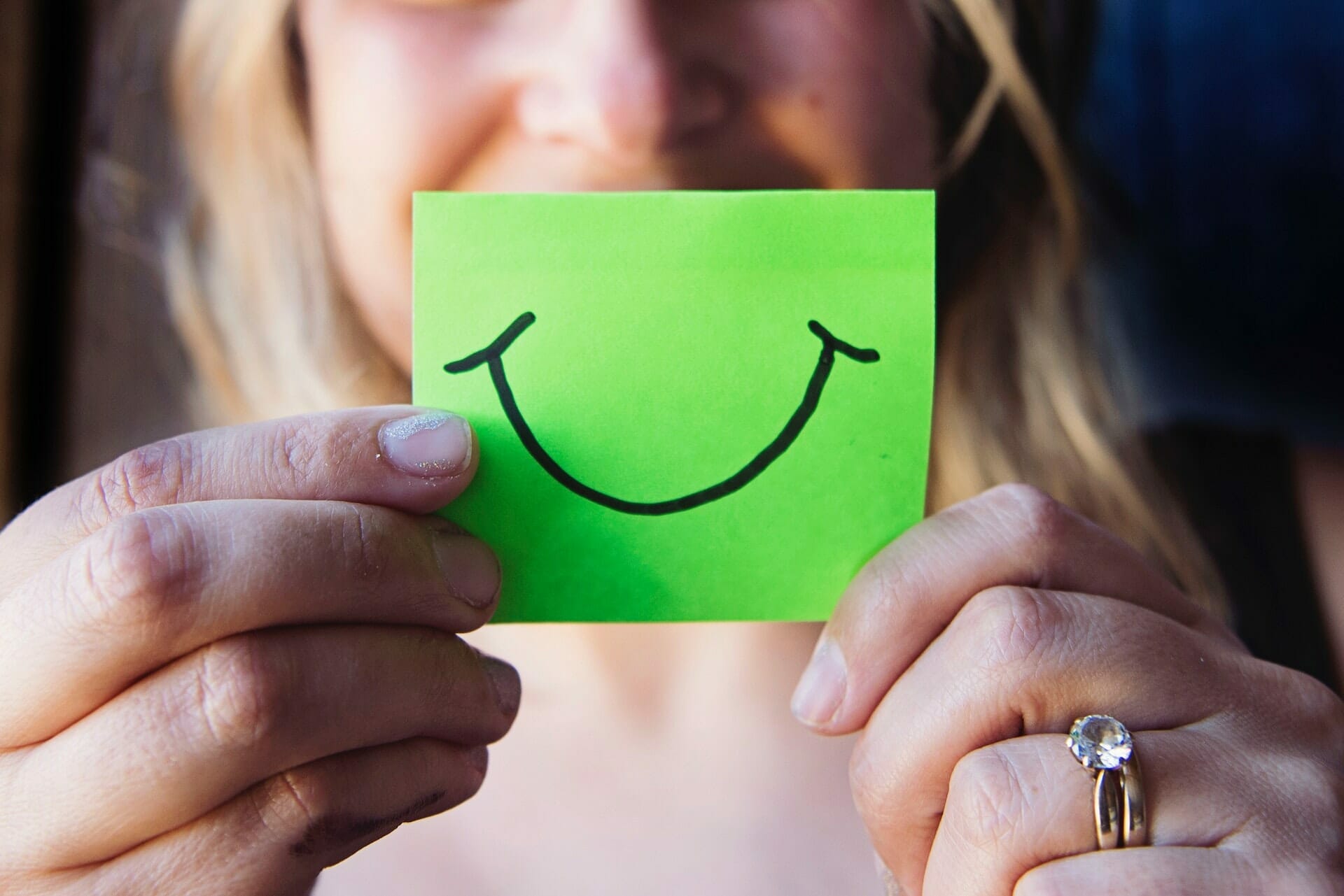 A woman holding a green post-it note with a smile drawn on it