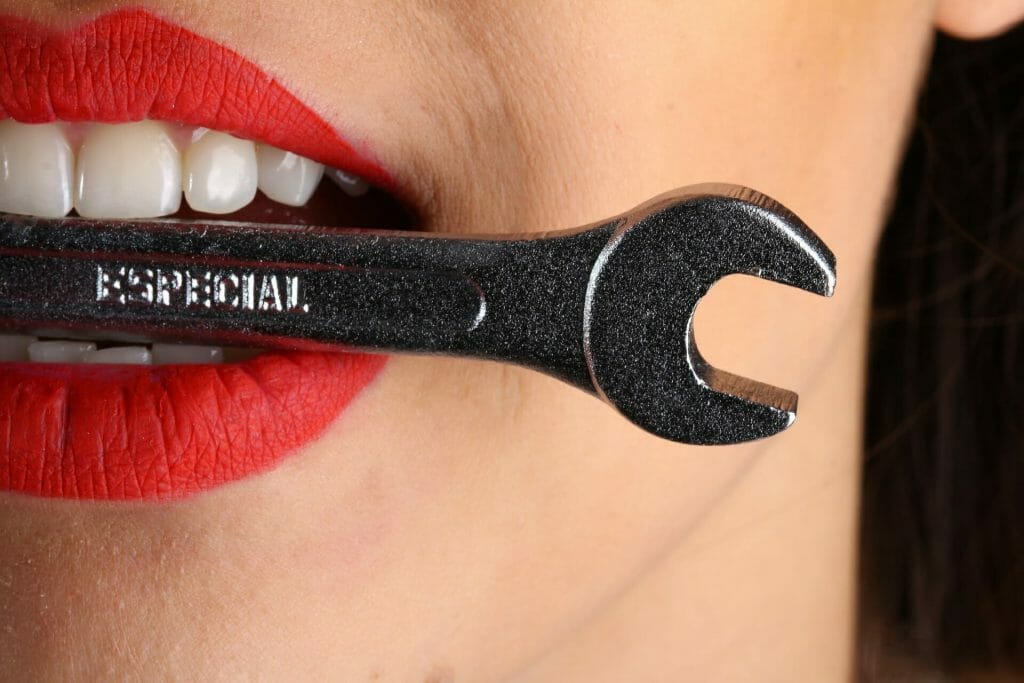 A woman with red lips holding a spanner between her teeth