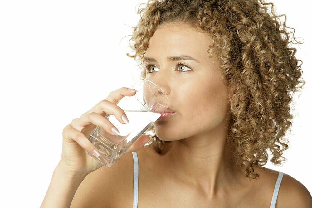 A woman with curly hair drinking a glass of water